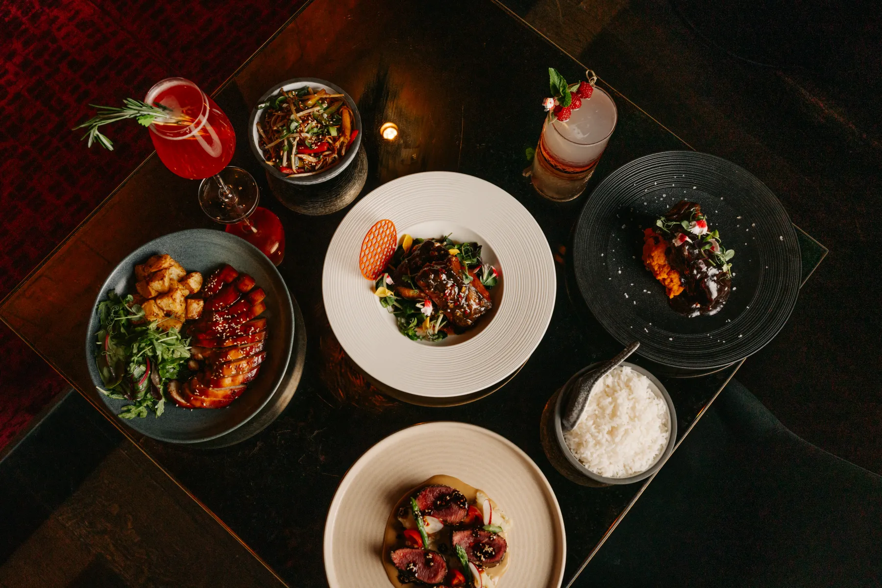 Sesame glazed chicken, wok-fried noodles, sliced beef and cocktails on a table at Lulu Wild, Chinese restaurant and cocktail bar in Birmingham